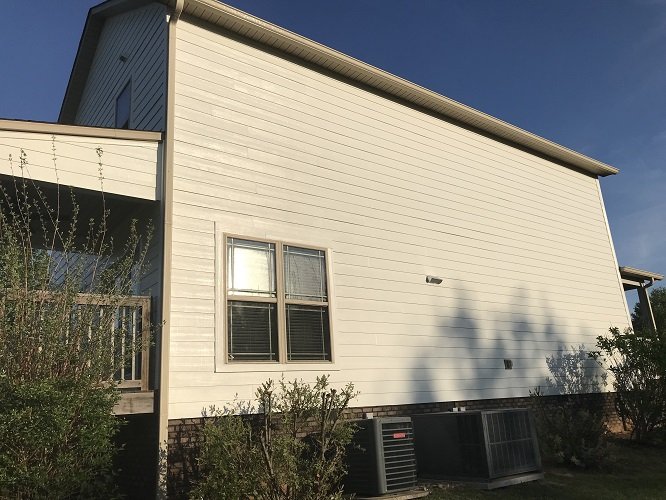 Freshly painted white siding on the side of a two-story house under a blue sky