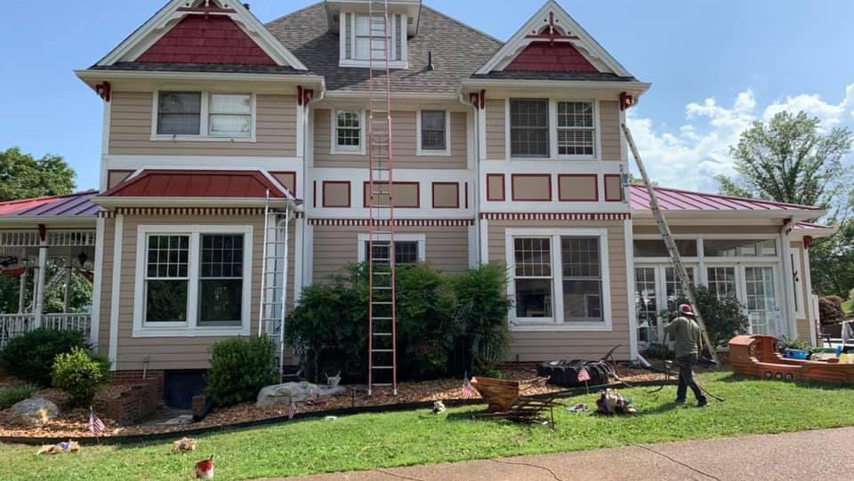 Two-story Victorian house exterior repaint in progress with ladders