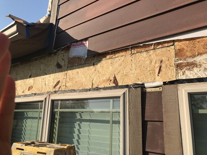 Damaged siding and plywood above a window exposed for repair before painting
